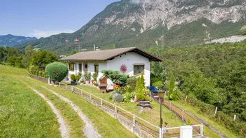 Haus in alpiner Landschaft mit Bergblick und gepflegtem Gartenbereich unter blauem Himmel.