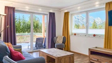 Helles Wohnzimmer mit Holzboden, Zugang zum Balkon und beeindruckendem Bergblick.