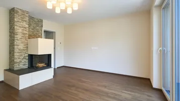 Geräumiges Wohnzimmer mit modernem Kamin, dunklem Holzboden und großen Fenstern.