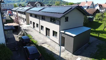 Reihenhäuser mit moderner Architektur und Photovoltaikanlagen auf den Dächern in ländlicher Umgebung.