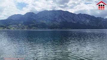 Panoramablick auf einen malerischen See mit majestätischen Bergen im Hintergrund unter bewölktem Himmel.