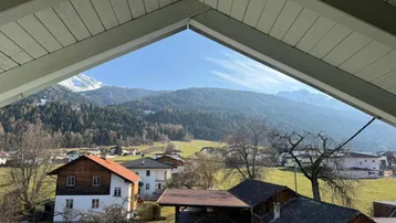 Bergblick aus einem Dachzimmer mit Holzbalken und weitem Ausblick auf die umliegende Landschaft.