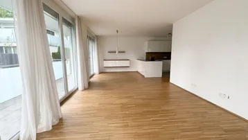 Helles Wohnzimmer mit Parkettboden, großen Fensterfronten und offenem Zugang zur Küche.
