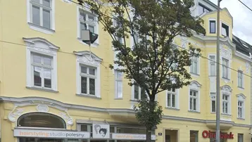 Historisches Mehrfamilienhaus mit gelber Fassade, Geschäften im Erdgeschoss und Wohnungen in den oberen Etagen.