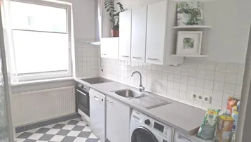 Helle Küche mit weißen Fliesen, Schachbrettboden und integrierter Waschmaschine unter der Arbeitsplatte.