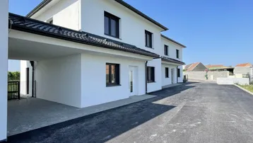 Neues weißes Gebäude mit modernem Design, Carport und asphaltierter Zufahrt unter blauem Himmel.