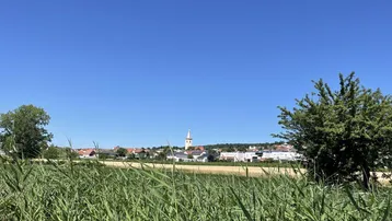 Weite ländliche Landschaft mit Feldern und einem Dorf mit Kirchturm in der Ferne.