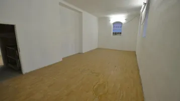 Leerer Raum mit hellen Holzböden und einem kleinen vergitterten Fenster, bereit zur individuellen Gestaltung.