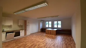 Geräumiger Büroraum mit integrierter Küchenzeile, großen Fenstern und Laminatboden.