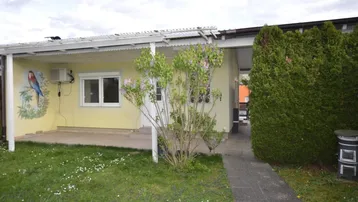 Vorderansicht eines Hauses mit kleiner Rasenfläche, überdachtem Eingangsbereich und Wandmalerei.