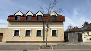 Traditionelles Haus mit beiger Fassade und Mansarddach, typisch für die ländliche Architektur.