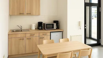 Helle Küchenzeile mit Holzschränken, Mikrowelle und Essbereich, ideal für Pausen.