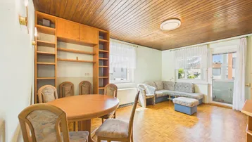 Geräumiger Wohn- und Essbereich mit Holzdecke, Parkettboden und Zugang zum Balkon.