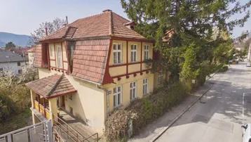 Historisches Gebäude mit Mansarddach und gelber Fassade an einer ruhigen Straße gelegen.
