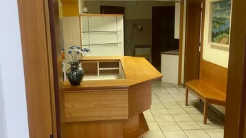 Blick in einen Empfangsbereich mit Holztheke, Regalen und gefliestem Boden.