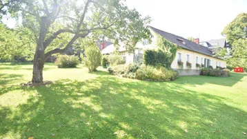 Weitläufiger Garten mit altem Baumbestand und Blick auf das traditionelle Landhaus.