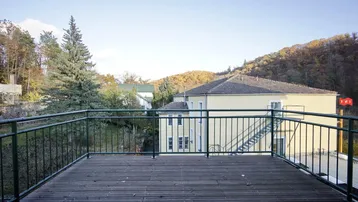 Geräumige Holzterrasse mit Metallgeländer und weitem Blick über eine grüne Landschaft.