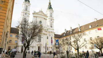 Historische Kirche mit zwei Türmen an einem belebten Platz in einer europäischen Stadt.