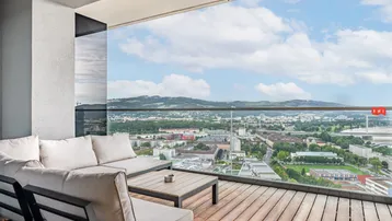 Geräumiger Balkon mit bequemen Loungemöbeln und weitem Blick über die Stadt und Berge.