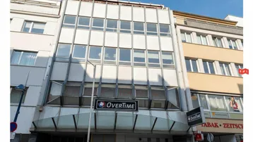 Fassade eines Geschäftsgebäudes mit großen Fenstern und Werbeschildern in einer städtischen Umgebung.