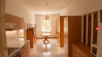 Helles Zimmer mit integrierter Küchenzeile, Holzboden und einem Tisch in der Mitte.