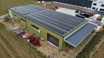 Luftaufnahme eines modernen Gewerbegebäudes mit Photovoltaikanlage auf dem Dach und umliegendem Gelände.