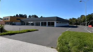 Modernes Geschäftsgebäude mit großen Fensterfronten und weitläufigem Parkplatz unter blauem Himmel.