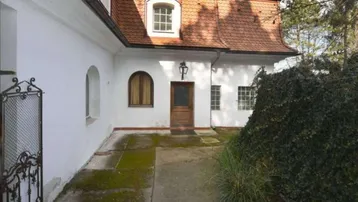 Historisches Gebäude mit weißer Fassade, roten Dachziegeln und einem charmanten Holzeingang.