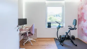 Vielseitiger Raum, genutzt als Büro und Fitnessbereich, mit Blick ins Grüne.