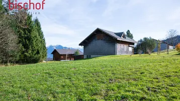 Ländliche Umgebung mit traditionellem Gebäude und weitem Blick auf die Berge unter blauem Himmel.