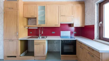 Funktionale Küche mit hellen Holzschränken, roter Rückwand und integriertem Backofen.