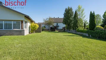 Großer, gepflegter Garten mit Rasenfläche und Blick auf das Wohnhaus unter blauem Himmel.