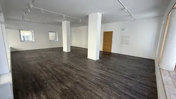 Geräumiger, leerer Gewerberaum mit dunklem Holzboden, weißen Wänden und Säulen, ideal für Laden oder Büro.