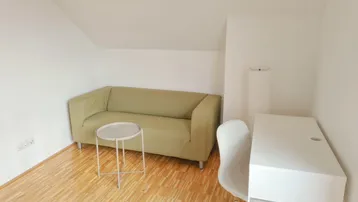 Helles Zimmer im Dachgeschoss mit Sofa, Schreibtisch und Holzfußboden.