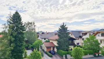 Blick über eine Wohnsiedlung mit Häusern, Bäumen und einer Straße unter bewölktem Himmel.