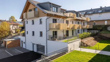 Modernes Mehrfamilienhaus mit Balkonen, Terrassen, Tiefgarage und gepflegten Grünflächen in sonniger Lage.