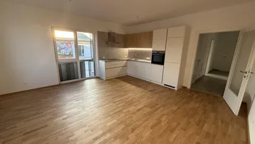 Heller offener Wohnbereich mit moderner Einbauküche, Parkettboden und Zugang zum Balkon.