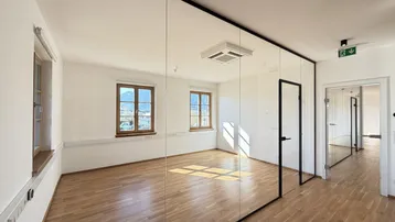 Heller Büroraum mit modernen Glaswänden, Holzboden und Blick auf die umliegende Landschaft.