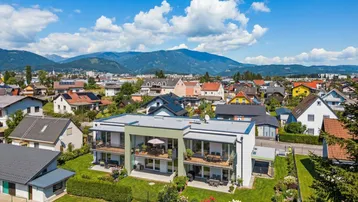 Moderne Wohnanlage mit Balkonen und Terrassen, umgeben von Grünflächen und Bergblick.