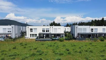 Moderne Reihenhäuser in ländlicher Umgebung mit Blick auf grüne Felder und Berge.