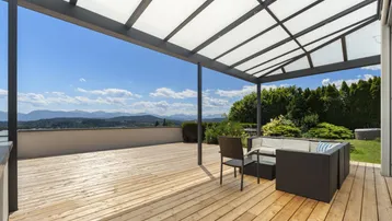 Geräumige überdachte Holzterrasse mit Sitzgelegenheiten und weitem Blick auf die Berge.