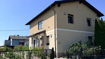 Einfamilienhaus mit beiger Fassade, Satteldach und gepflegtem Vorgarten unter blauem Himmel.