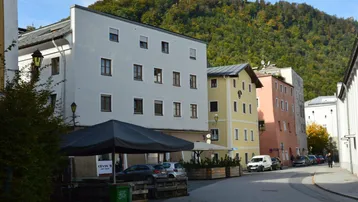 Blick auf eine belebte Straße mit mehrstöckigen Gebäuden und bewaldeten Bergen im Hintergrund.