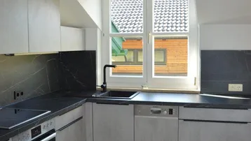 Moderne Küche mit grauen Schränken, dunkler Arbeitsplatte und Dachfenster.