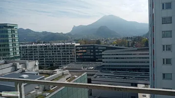 Weitläufiger Blick über die Stadtlandschaft mit Bergen im Hintergrund von einem oberen Stockwerk.