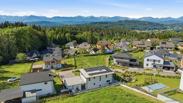 Luftaufnahme der Wohnsiedlung mit Bergen im Hintergrund und viel Grün.