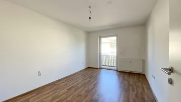 Helles Zimmer mit Parkettboden und Zugang zu einem französischen Balkon.
