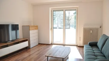 Helles Wohnzimmer mit Parkettboden, Sofa und Zugang zu einem Balkon oder einer Terrasse.