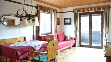 Gemütlicher Wohn- und Essbereich im alpinen Stil mit Holzbalkendecke und Zugang zum Balkon.