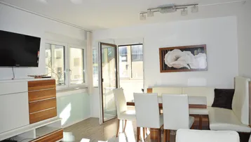 Helles Wohn- und Esszimmer mit modernem Mobiliar, Holzakzenten und Zugang zum Balkon.